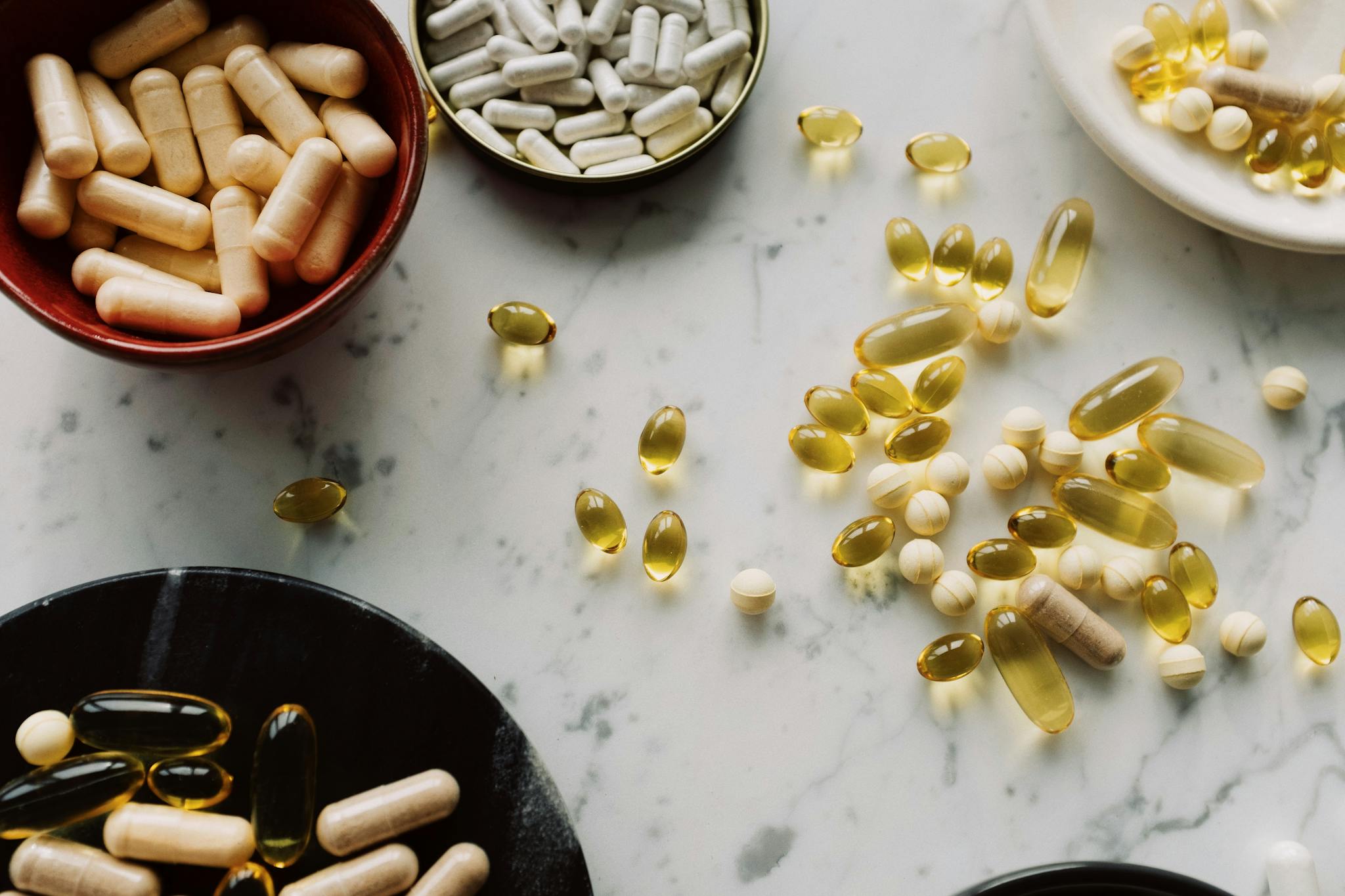 A flat lay of diverse capsules and supplements on a marble countertop, showcasing health and wellness products.
