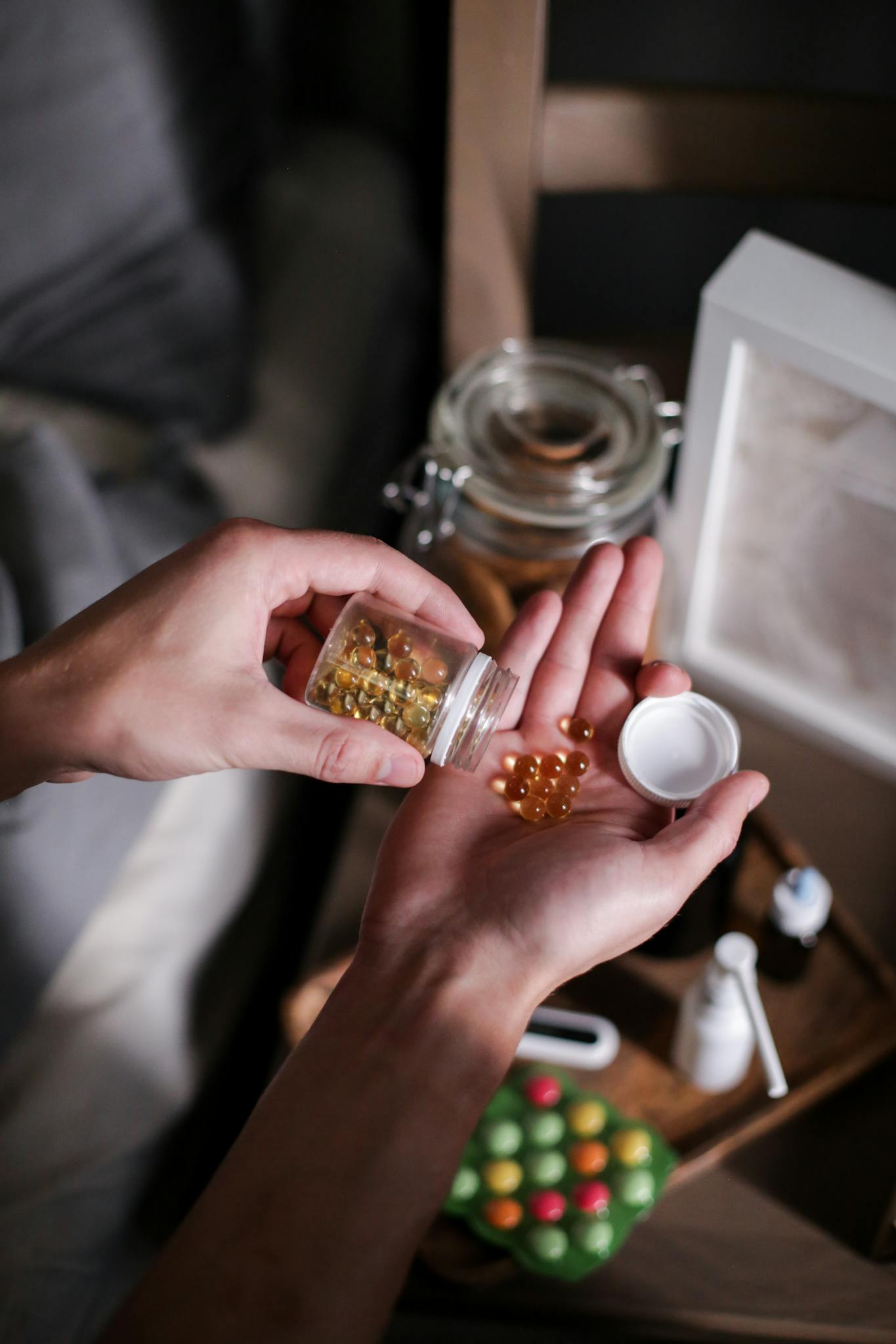Close-up of hands pouring vitamin capsules from a bottle, emphasizing health routines.