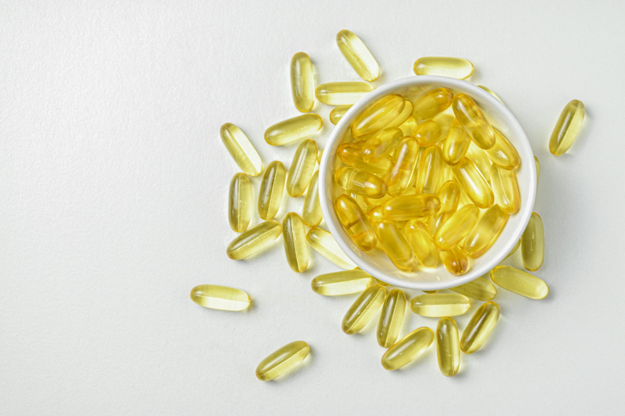 High-angle shot of omega-3 fish oil capsules in a ceramic bowl on a white background.